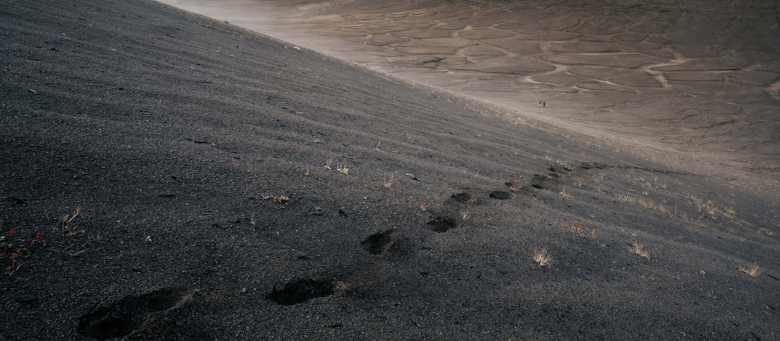 Dry, hilly landscape with visible footprints on the ground from people walking in the distance.