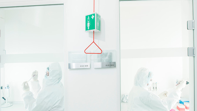 Two reseachers working in small, separate labs, wearing protective gear.